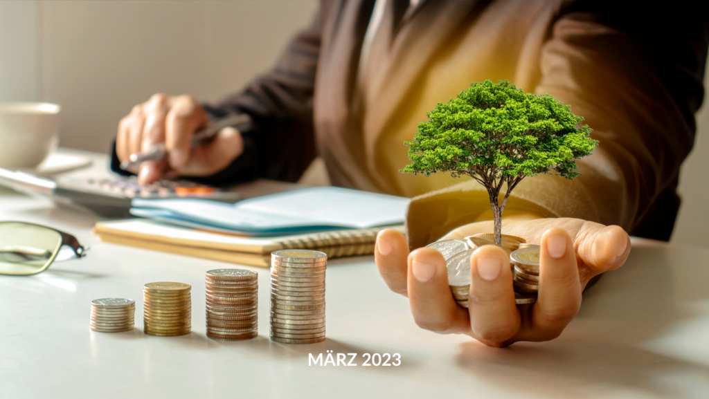 Eine Person an einem Schreibtisch, die die Finanzen für die neue KfW-Förderung berechnet, hält einen kleinen Baum, der aus einem Haufen Münzen wächst und das Investitionswachstum symbolisiert. Der Text lautet: „Mär