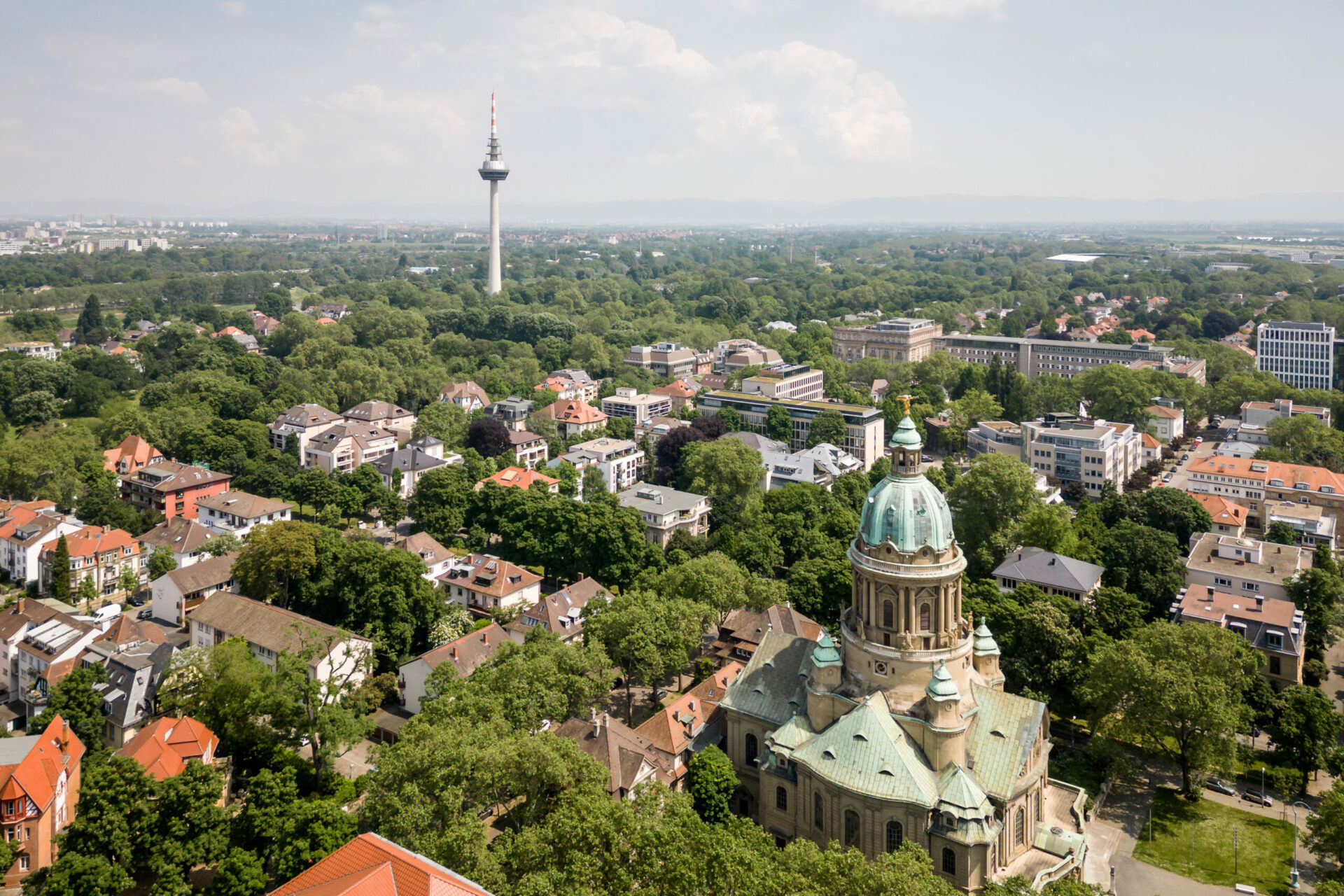 Luftaufnahme der Oststadt mit einer Mischung aus Bäumen, Wohngebäuden und einer markanten historischen Kirche sowie einem hohen Sendeturm im Hintergrund.