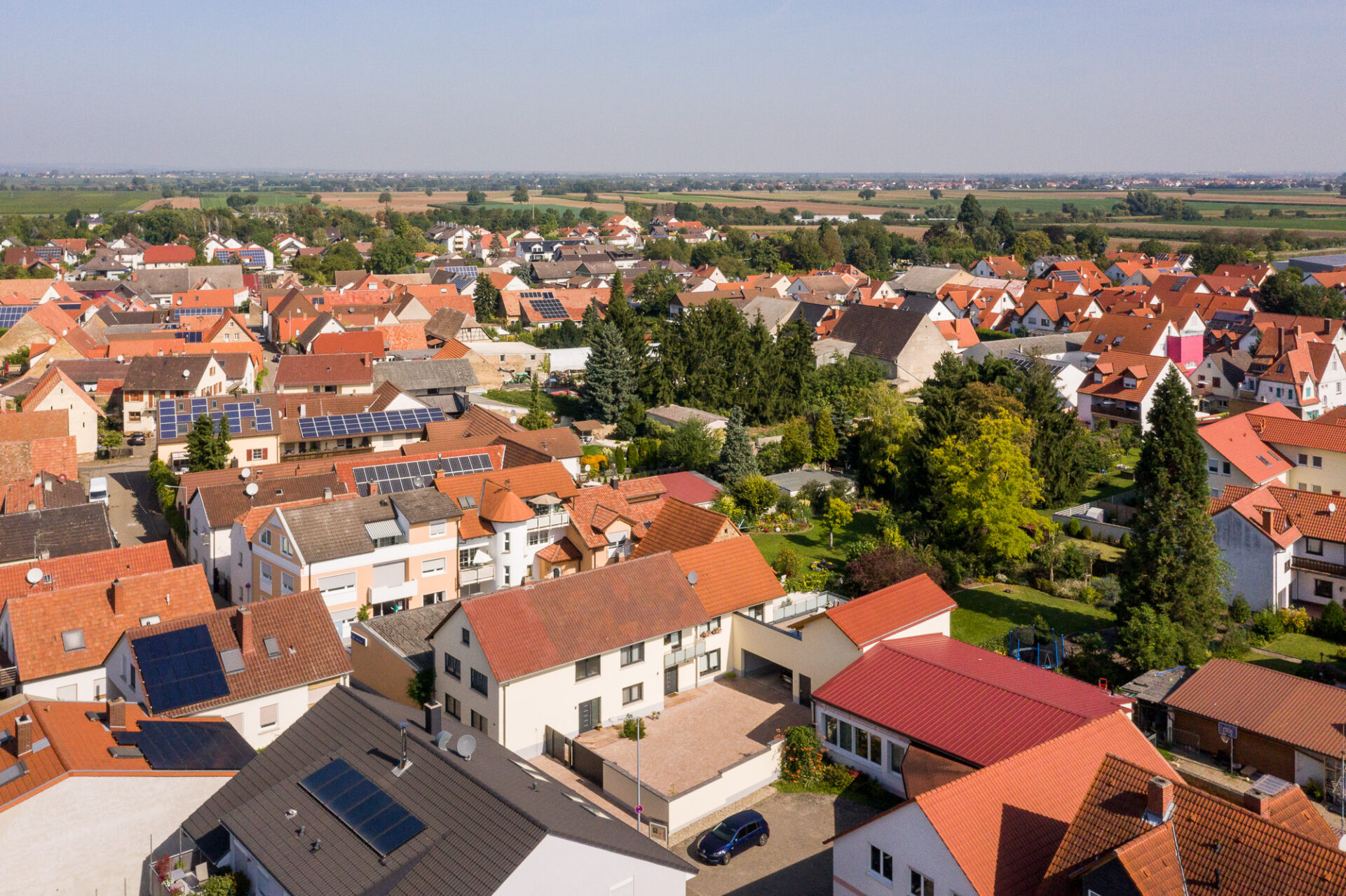 Luftaufnahme eines Vorortviertels in Meckenheim mit dicht gedrängten Häusern mit Solarmodulen, umgeben von flachem Ackerland.