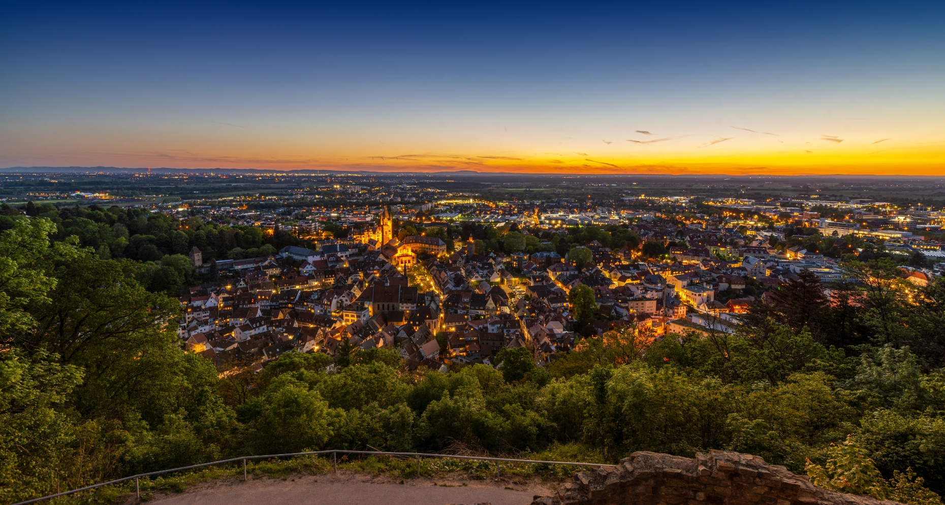 Ein Panoramablick auf eine Stadt bei Sonnenuntergang mit beleuchteten Gebäuden und einer Kathedrale, einem weiten Himmel und einem fernen Horizont. Diese Szene symbolisiert die Essenz der Teamarbeit, da verschiedene Strukturen harmonisch koexistieren