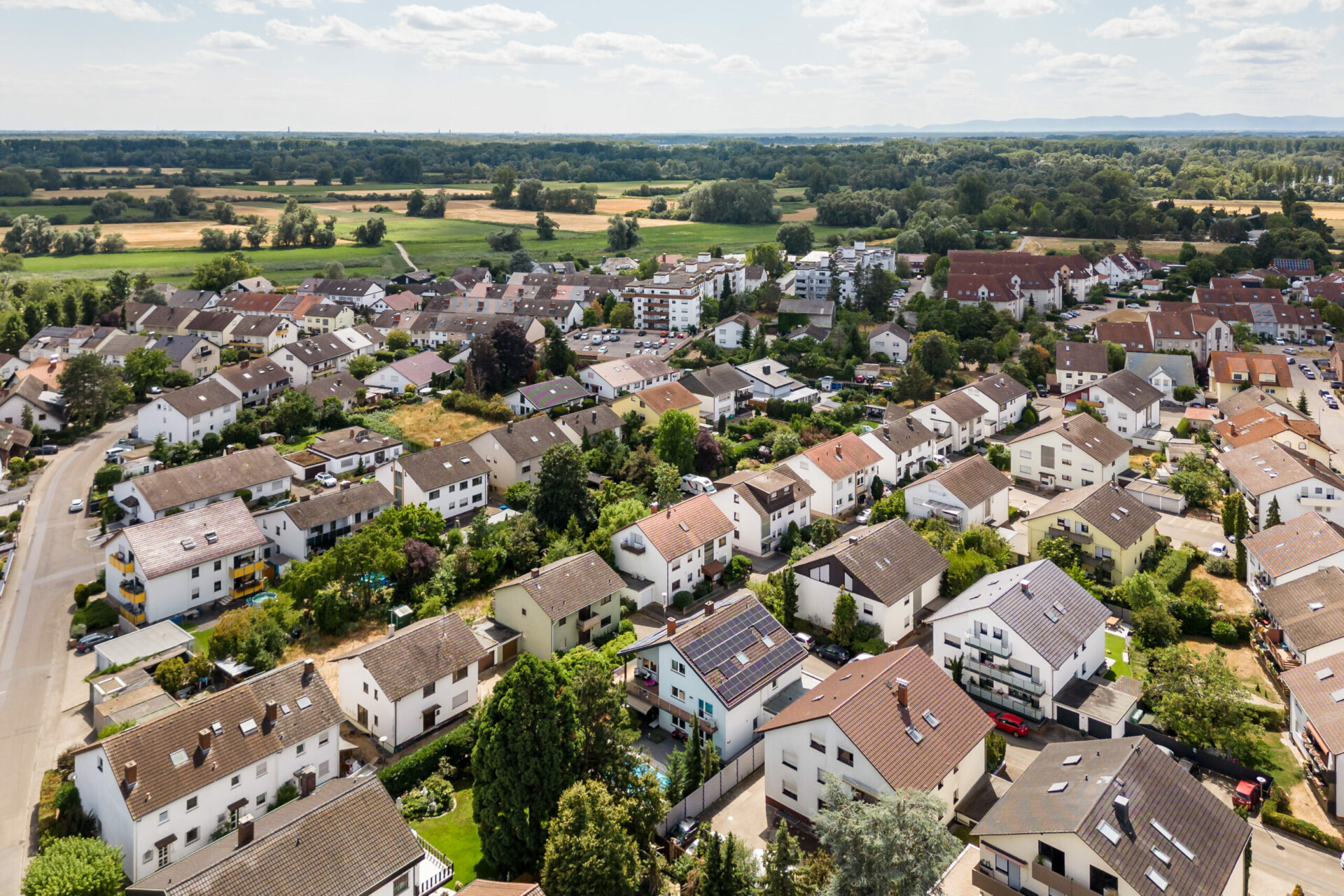 Luftaufnahme des Stadtteils Brühl mit seinen dicht gedrängten weißen Häusern, umgeben von grünen Feldern und einem klaren Himmel.