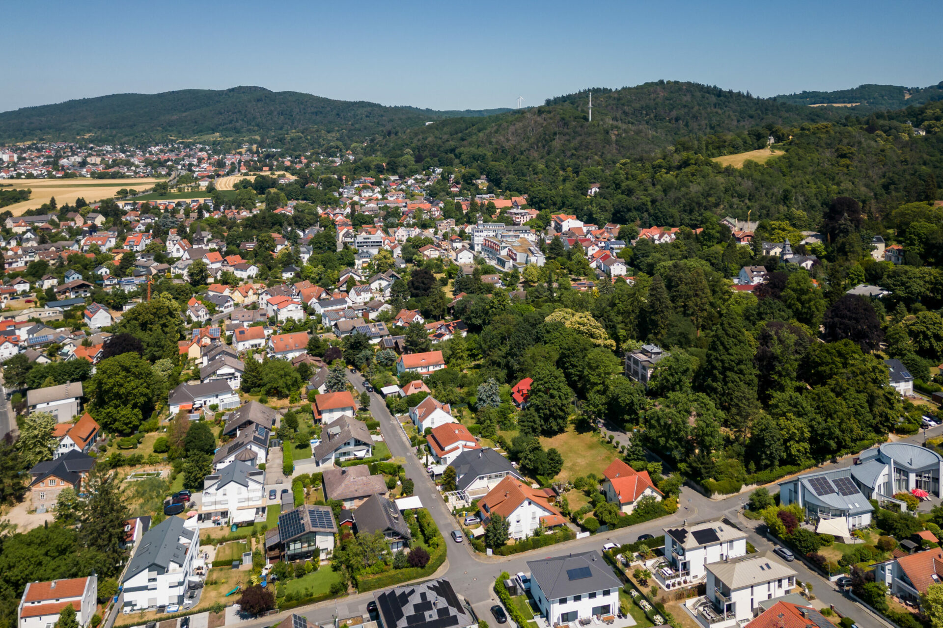 Luftaufnahme von Seeheim-Jugenheim mit ordentlichen Häuserreihen, grünen Bäumen und sanften Hügeln im Hintergrund an einem sonnigen Tag.