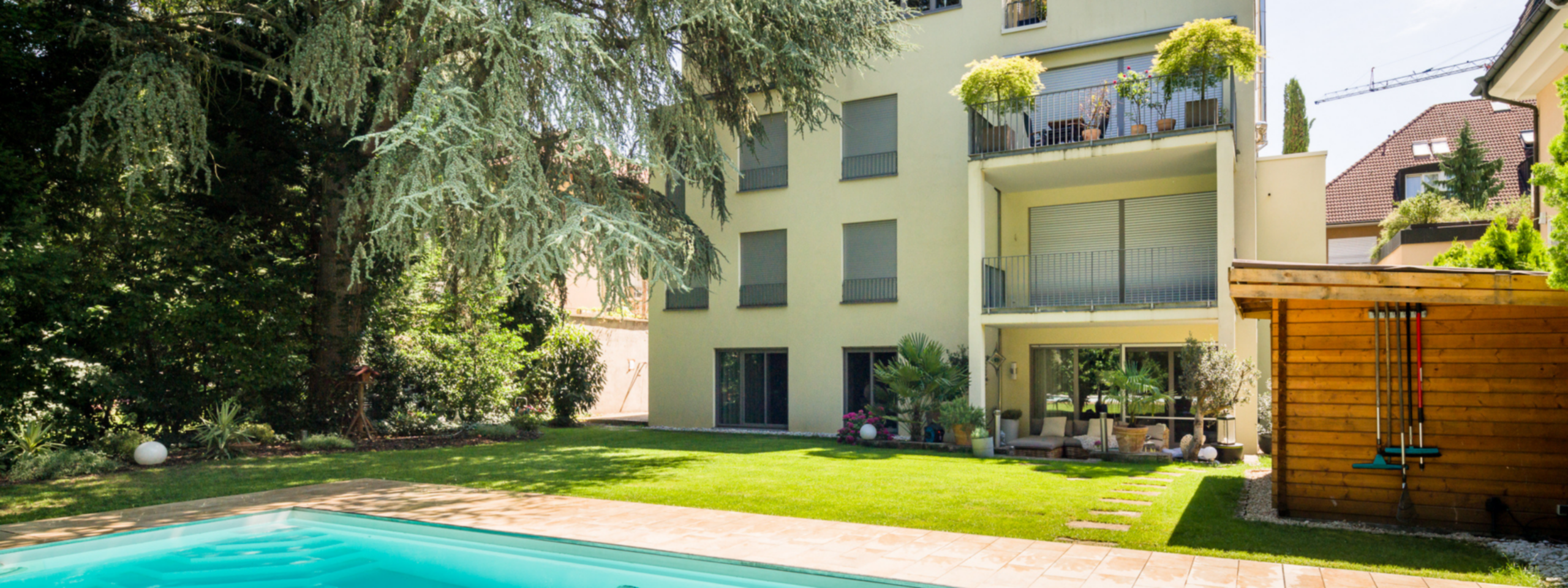 Modernes mehrstöckiges Apartmentgebäude mit Balkonen mit Blick auf einen Swimmingpool und Garten in sonniger Lage.