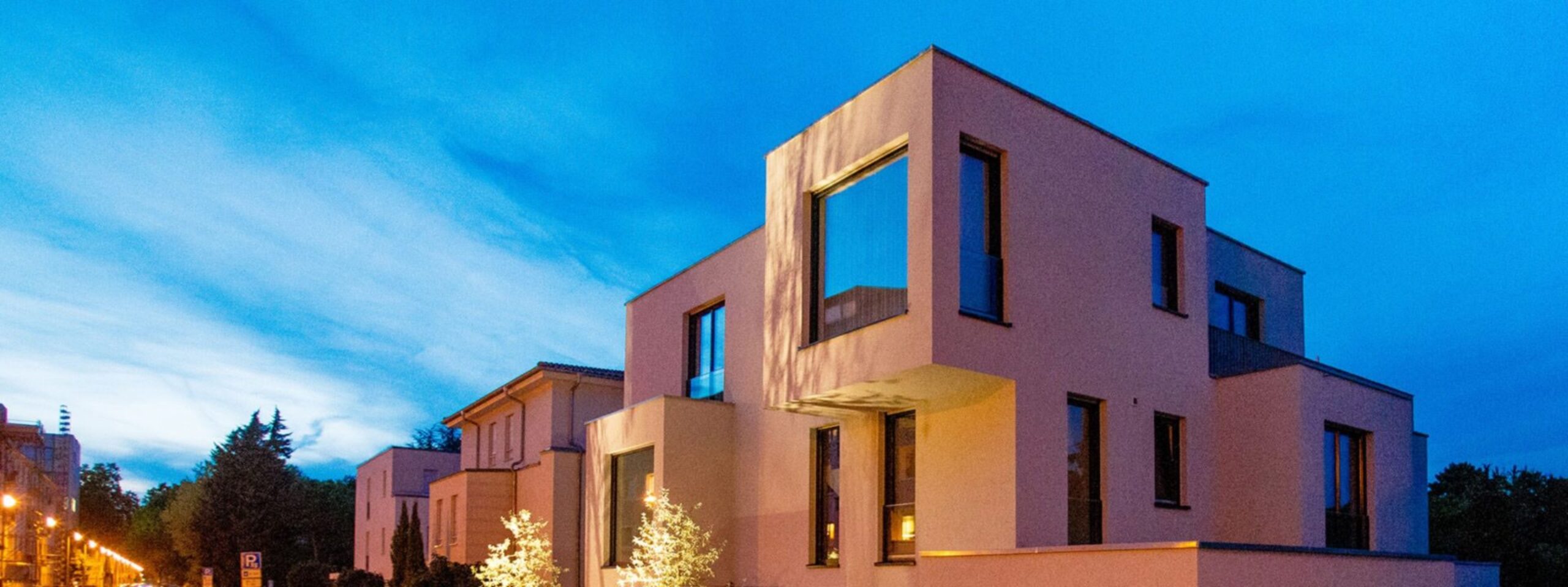 Moderne kubische Architektur eines Gebäudes, das in der Dämmerung unter einem blauen Himmel beleuchtet wird.